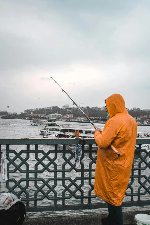 a person standing on a bridge with a fishing rod, by Nazmi Ziya Güran, pexels contest winner, hyperrealism, orange jacket, istanbul, fish seafood markets, yellow raincoat