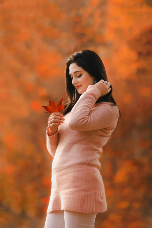 a woman standing in a field holding a leaf, a picture, by irakli nadar, pexels contest winner, long orange sweatshirt, cute elegant pose, 15081959 21121991 01012000 4k, pink and red colors