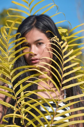 a woman standing in front of a palm tree, by Robbie Trevino, trending on pexels, photorealism, portrait of modern darna, fern, beauty campaign, middle close up composition