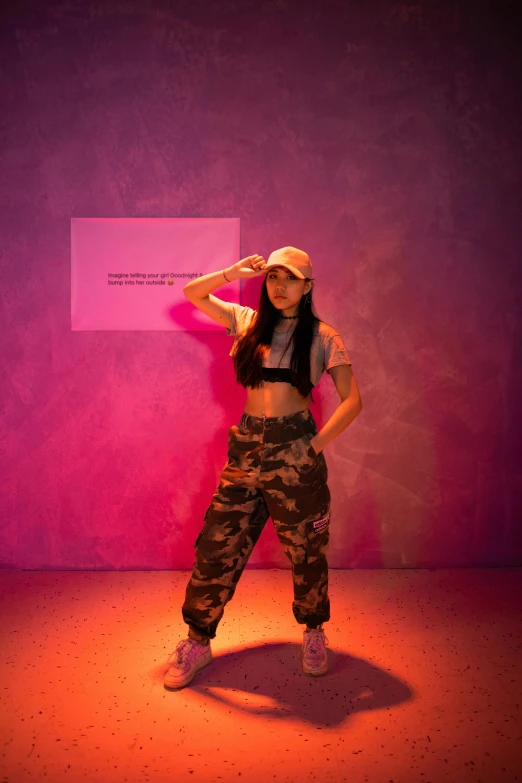 a woman standing in front of a pink wall, an album cover, inspired by Wang Meng, trending on pexels, holography, wearing cargo pants, on display in a museum, in fighter poses, wearing a chocker and cute hat