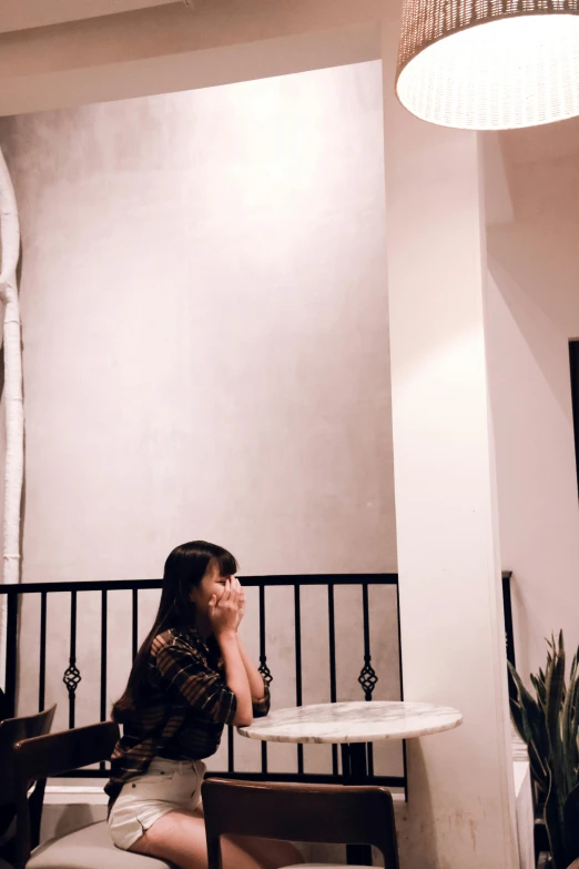 a woman sitting at a table talking on a cell phone, unsplash, ☁🌪🌙👩🏾, low quality photograph, minimalist photo, mysterious coffee shop girl