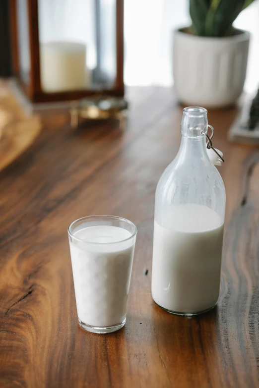 a bottle of milk next to a glass of milk, by Everett Warner, on wooden table, medium, full frame image, ivory