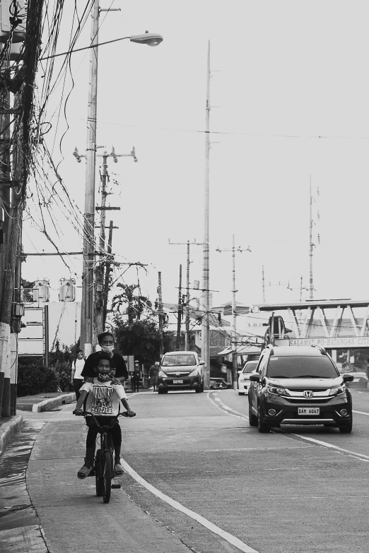 a person riding a bike down a street, a black and white photo, by Willie Ito, unsplash, philippines, power lines, square, lonely family