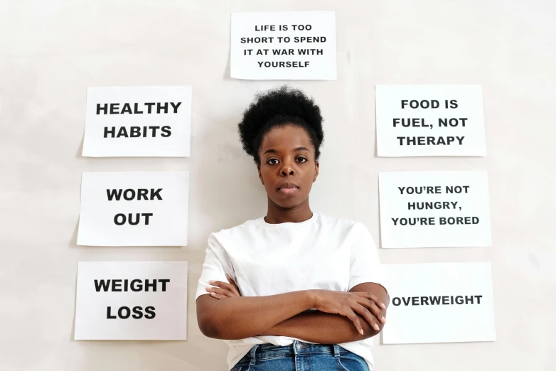 a woman standing in front of a wall with signs on it, by Olivia Peguero, pexels contest winner, on a white table, health, black young woman, on a pale background