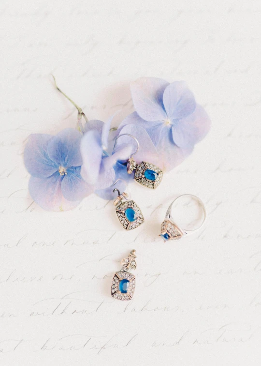 a pair of earrings sitting on top of a piece of paper, renaissance, blue flowers accents, thumbnail, rings, dreamy style