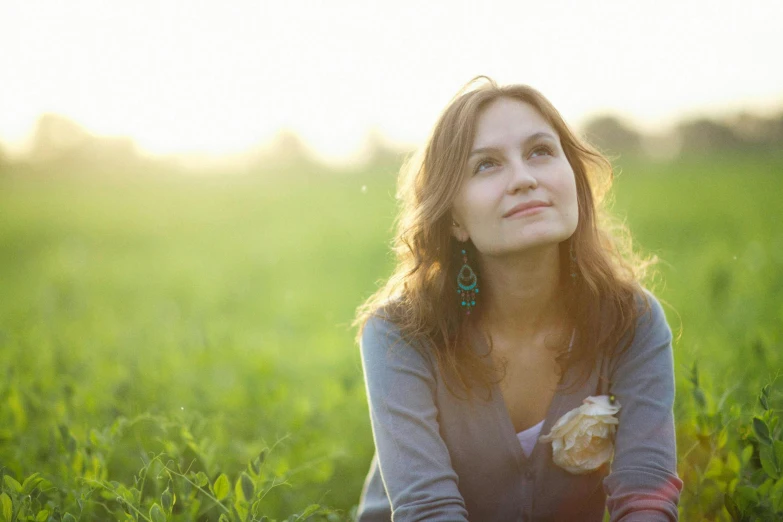 a woman sitting on top of a lush green field, profile image, light behind, portrait image, compassionate