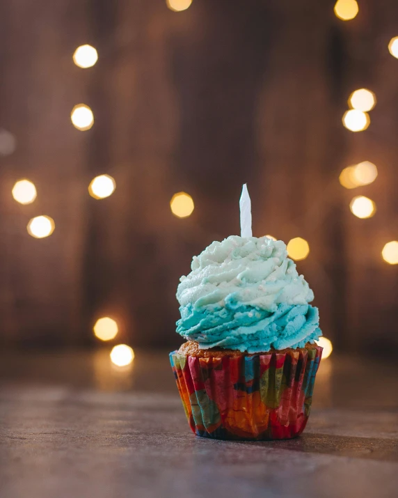 a cupcake with a single candle on top of it, by Elsa Bleda, trending on unsplash, blue and green and red tones, barbarian celebrate his birthday, non-binary, white and teal metallic accents