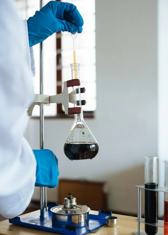 a person in a lab coat holding a beaker filled with liquid, inspired by Ceferí Olivé, unsplash, brown and cyan blue color scheme, sri lanka, hanging, private school