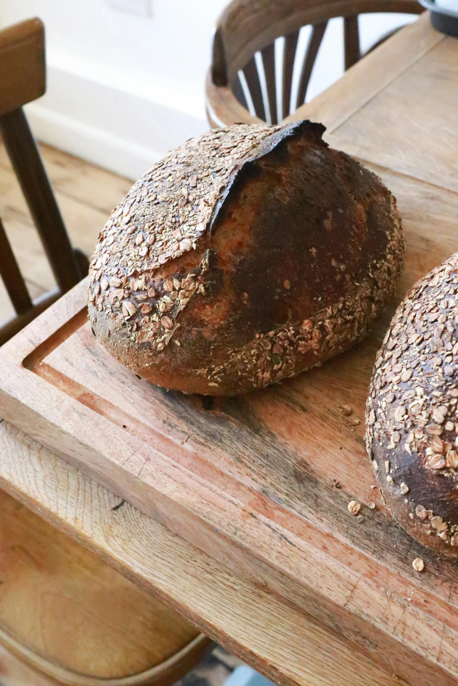 two loaves sitting on top of a wooden cutting board, by Helen Stevenson, seeds, oversized pauldrons, very crisp details, large head