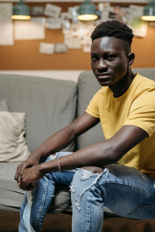 a man sitting on a couch in a living room, pexels contest winner, adut akech, lgbt, yellow hue, 18 years old
