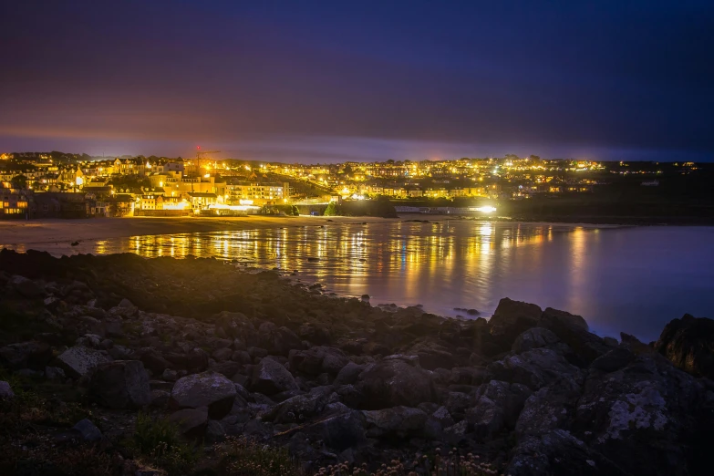 a large body of water surrounded by rocks, by Andrew Allan, pexels contest winner, nightime village background, pembrokeshire, shiny city in the distance, panorama