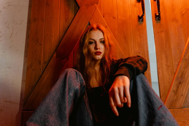 a woman sitting on the floor in front of a wooden door, a portrait, trending on pexels, antipodeans, orange skin and long fiery hair, concert, middle finger, in a cabin