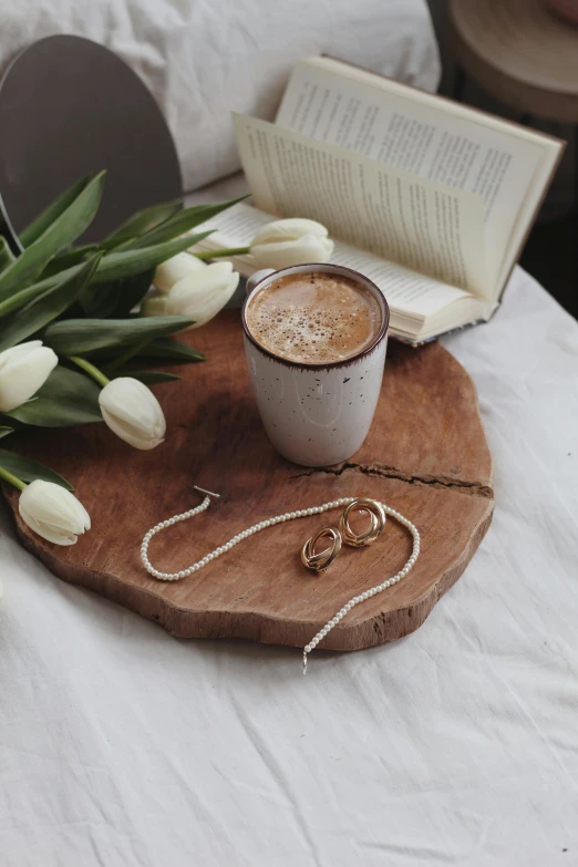 a cup of coffee sitting on top of a wooden tray, a still life, by Lucia Peka, trending on pexels, romanticism, tulips, necklace on display, brown and cream color scheme, sydney hanson