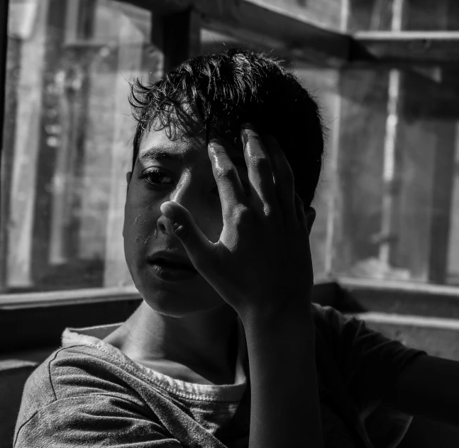 a black and white photo of a man talking on a cell phone, by Adam Marczyński, pexels contest winner, realism, portrait of depressed teen, 14 yo berber boy, harsh sunlight, near the window