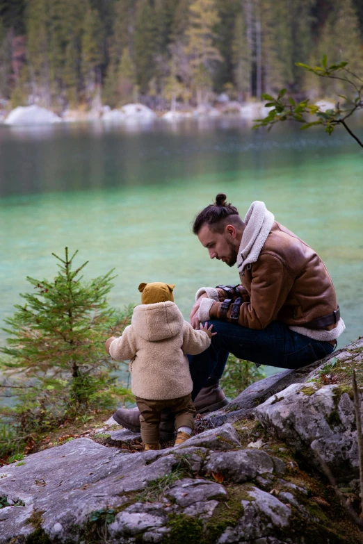 a woman sitting on a rock next to a teddy bear, fatherly, mini lake, kai carpenter, with a kid