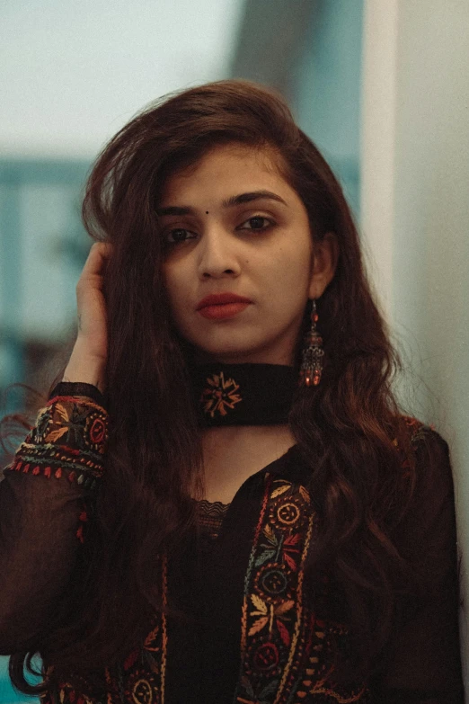 a woman in a black dress leaning against a wall, by Riza Abbasi, trending on pexels, wearing intricate black choker, wearing a kurta, young woman in her 20s, she has a distant expression