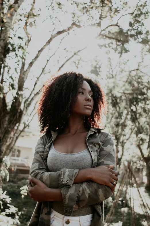 a woman standing in the woods with her arms crossed, pexels contest winner, renaissance, afro, sza, beautiful daylight, looking serious