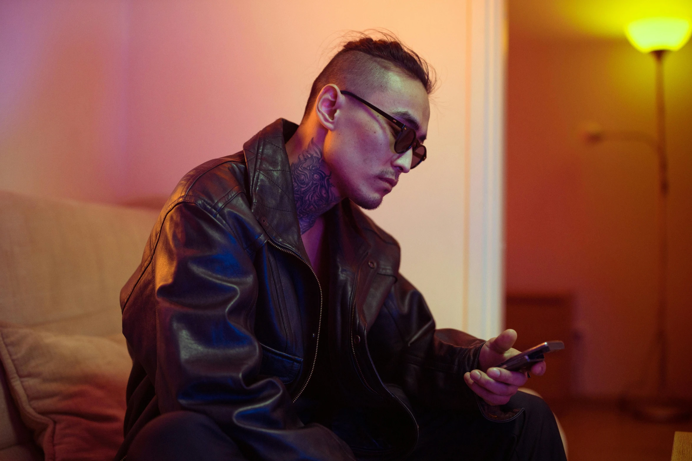 a man sitting on a couch holding a cell phone, inspired by Zhu Da, trending on pexels, visual art, slicked back hair, tattooed, wearing leather coat, bella poarch