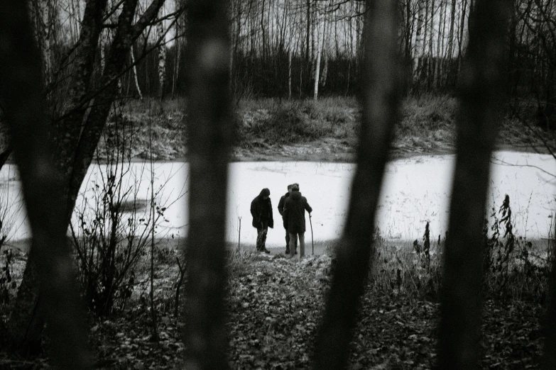 a couple of people that are walking in the snow, a black and white photo, by Jaakko Mattila, unsplash, visual art, in a swamp, blair witch project, hunting, medium format. soft light