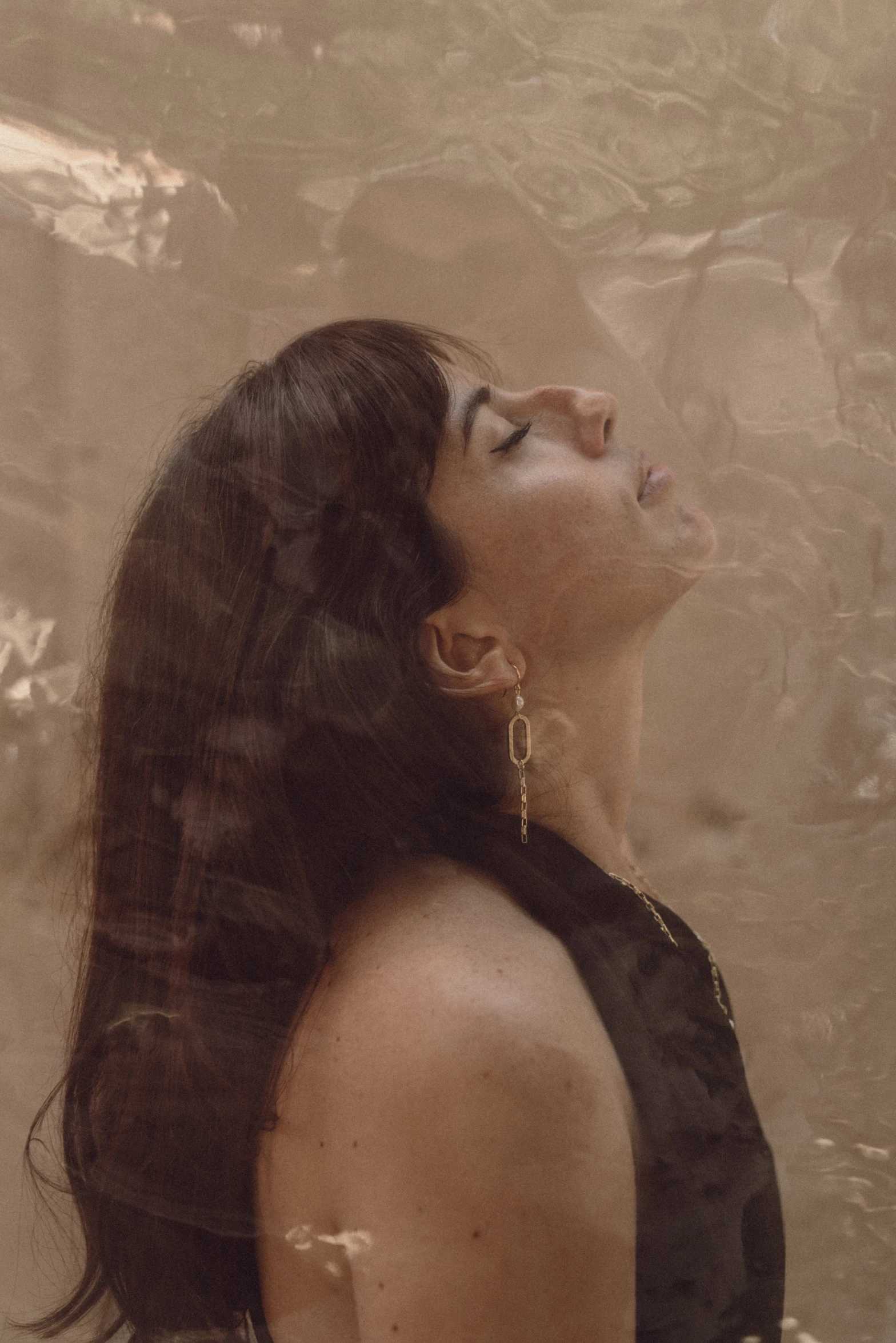 a woman in a black dress standing in front of a wall, an album cover, inspired by Elsa Bleda, trending on pexels, covered in transparent cloth, close - up profile face, still from a music video, yael shelbia