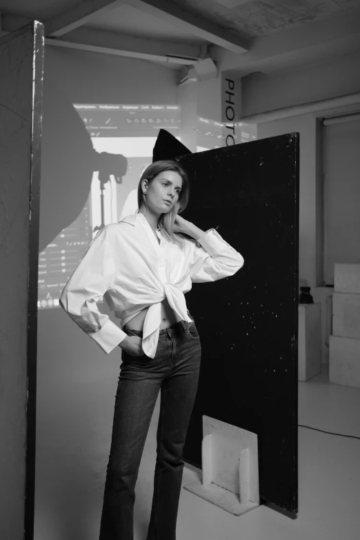 a black and white photo of a woman standing in front of a door, inspired by Peter Lindbergh, white shirt and jeans, anna kendrick, in a studio, wearing a white blouse