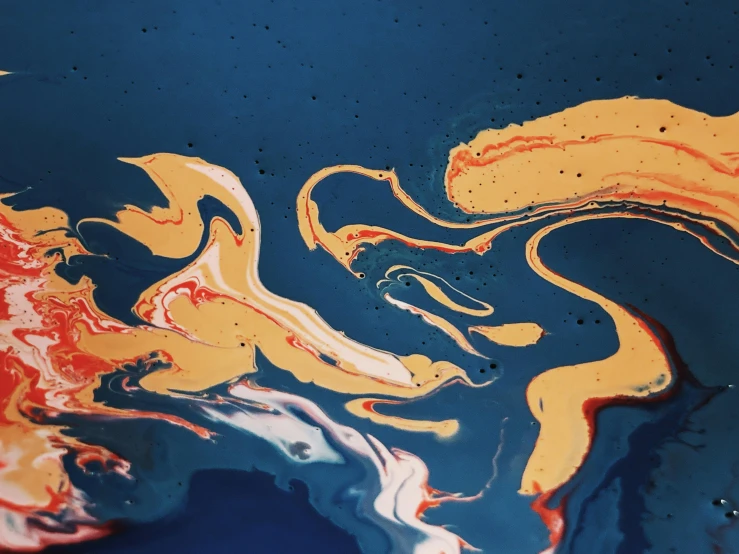 a close up of a painting on a surface, by Lee Loughridge, trending on unsplash, colors with gold and dark blue, floating liquid, james nares, some orange and blue