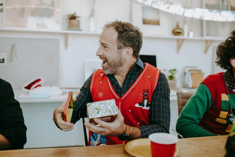 a group of people sitting around a wooden table, a photo, wearing festive clothing, profile image, smiling man, holding gift