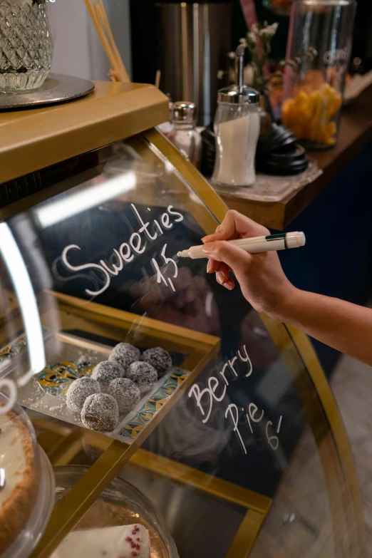 a woman is writing on a chalkboard in a bakery, a digital rendering, pexels, sweets, thumbnail, small, up close