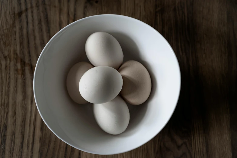 a white bowl filled with eggs on top of a wooden table, unsplash, various posed, jen atkin, grey, small