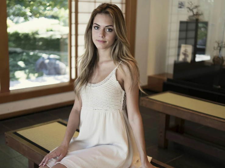 a woman sitting on a bench in a room, a portrait, unsplash, wearing a white sundress, wearing a camisole, meg kimura, young blonde woman