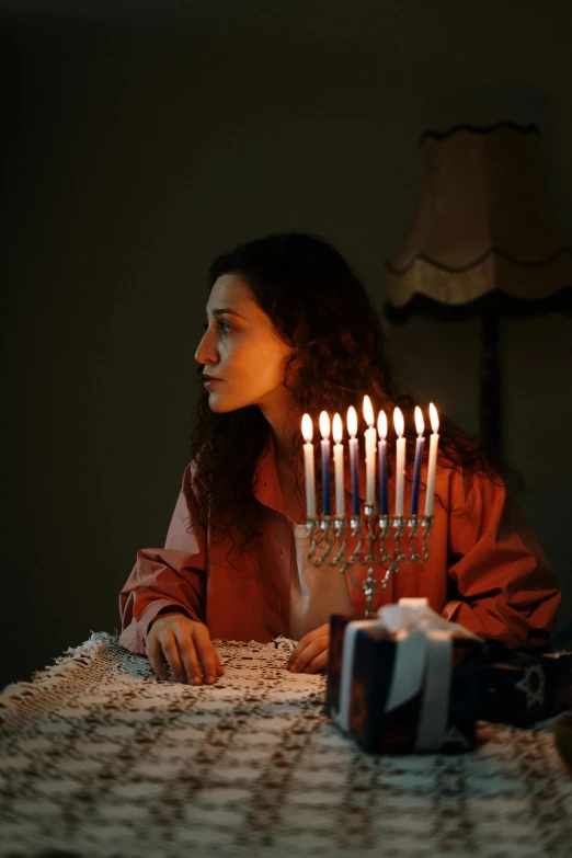 a woman sitting at a table with a lit menorah, inspired by Elsa Bleda, pexels, a person standing in front of a, holiday season, ( ( theatrical ) ), young middle eastern woman