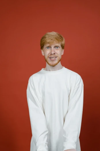 a man standing in front of a red wall, trending on reddit, realism, ginger hair, official government photo, wearing white clothes, catalog photo