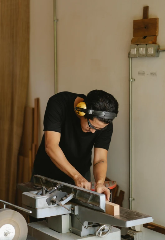 a man is working on a piece of wood, an album cover, inspired by Hiromitsu Takahashi, trending on unsplash, wood headphones hyperrealistic, asian male, architect studio, artist wearing overalls