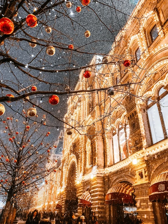 a group of people walking down a street next to a tall building, inspired by Vasily Surikov, pexels contest winner, baroque, christmas lights, profile image, ornate tiled architecture, during snowfall