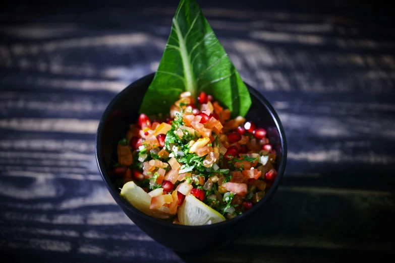 a bowl of food sitting on top of a wooden table, pomegranate, tropical leaves, relish, with a black background