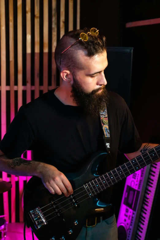 a man with a beard playing a guitar, profile image, bass sound waves on circuitry, looking towards camera, promo image