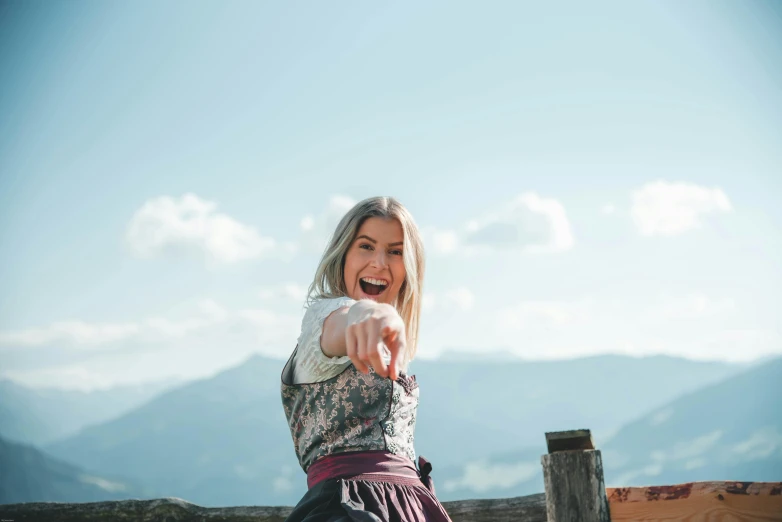 a woman standing on top of a wooden fence, by Niko Henrichon, pexels contest winner, she is smiling and excited, on the mountain, with pointing finger, avatar image