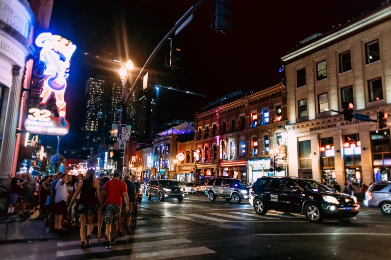 a crowd of people standing on the side of a street, by Carey Morris, pexels contest winner, city neon light, the city of toronto, background image, taverns nighttime lifestyle