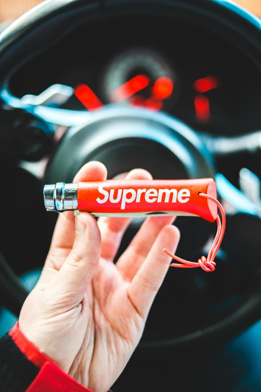a person holding a red pen in front of a steering wheel, inspired by Eugène Brands, trending on pexels, auto-destructive art, supreme, teddy fresh, smoke grenade, acronym