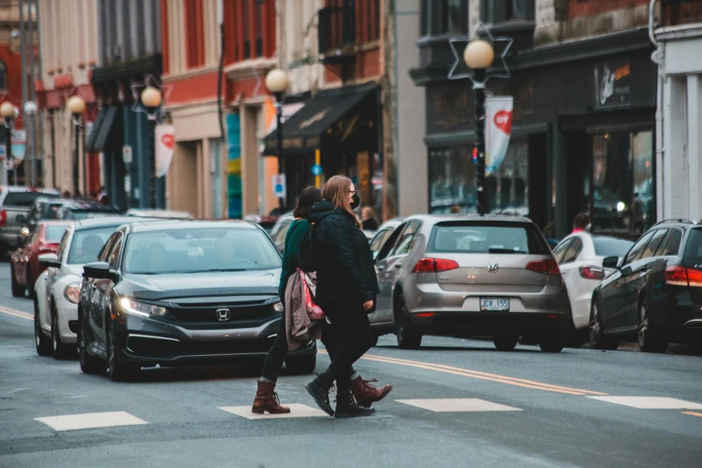 a man riding a skateboard down the middle of a street, pexels contest winner, woman holding another woman, car traffic, walking together, standing on street corner