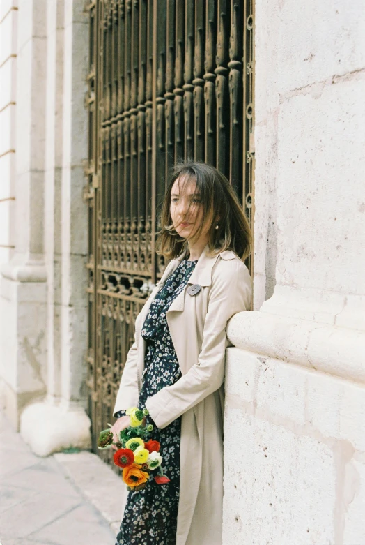 a woman leaning against a wall holding a bouquet of flowers, inspired by Modest Urgell, unsplash, ancient catedral behind her, wearing jacket, young asian woman, taken in the late 2000s