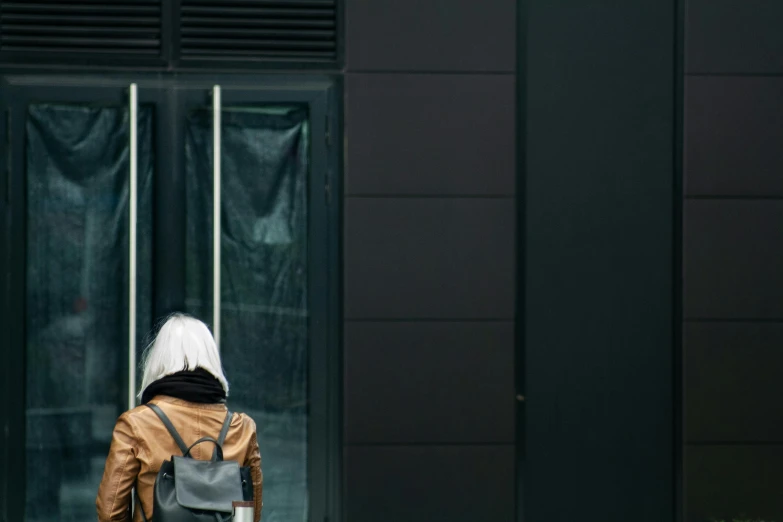 a person with a backpack standing in front of a building, inspired by Elsa Bleda, pexels contest winner, postminimalism, old lady cyborg merchant, about to enter doorframe, black and brown colors, silver haired