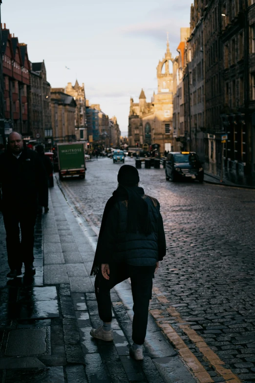 a group of people walking down a street next to tall buildings, an album cover, pexels contest winner, scotland, old city, wearing jeans and a black hoodie, view from the back