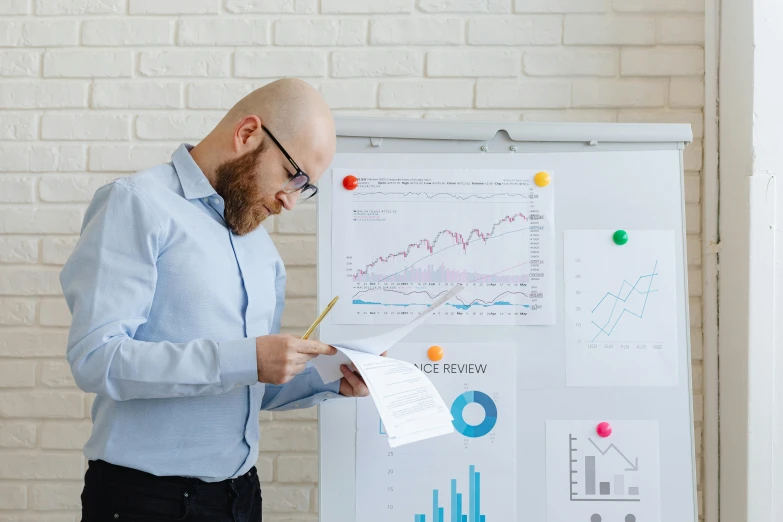 a man standing in front of a white board with graphs on it, pexels contest winner, papers on table, holding a clipboard, profile image, clear focused details