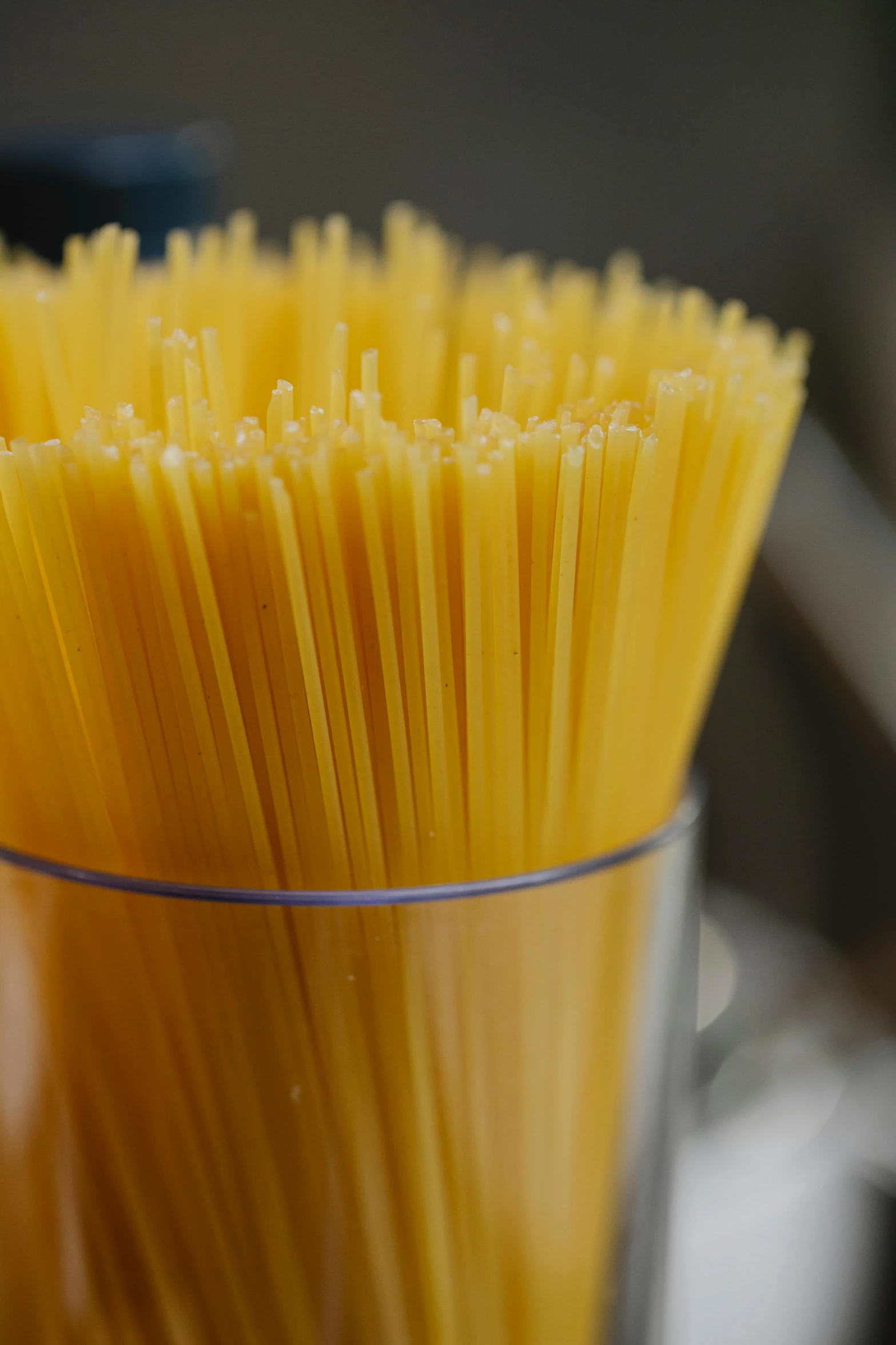 a glass filled with spaghetti noodles sitting on top of a counter, yellow, zoomed in, sleek spines, 王琛