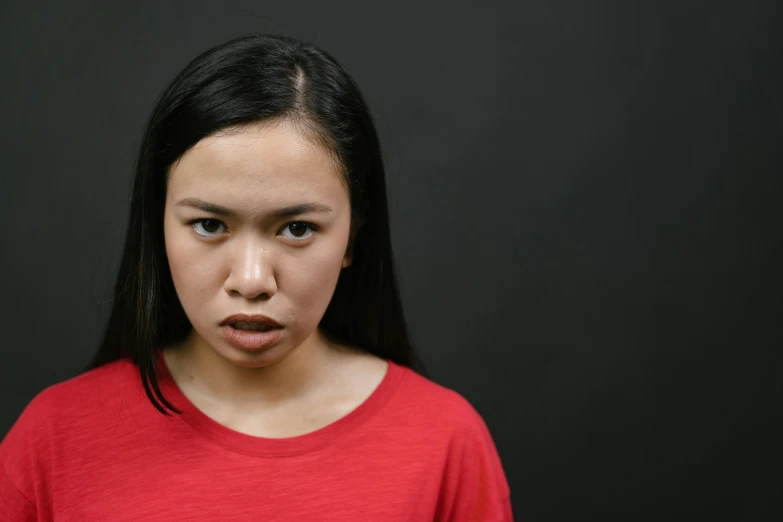 a woman with a surprised look on her face, pexels contest winner, mingei, red shirt, half asian, black backdrop, feeling of disgust