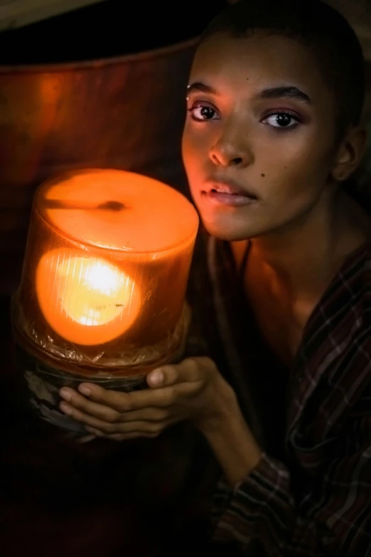 a woman holding a lit candle in her hand, inspired by Gordon Parks, orange lamp, with brown skin, promo image, girl under lantern
