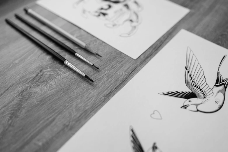 a couple of cards sitting on top of a wooden table, an ink drawing, trending on pexels, modern european ink painting, tattoo design sketch, bird tattoo, behance art, painted with a thin brush