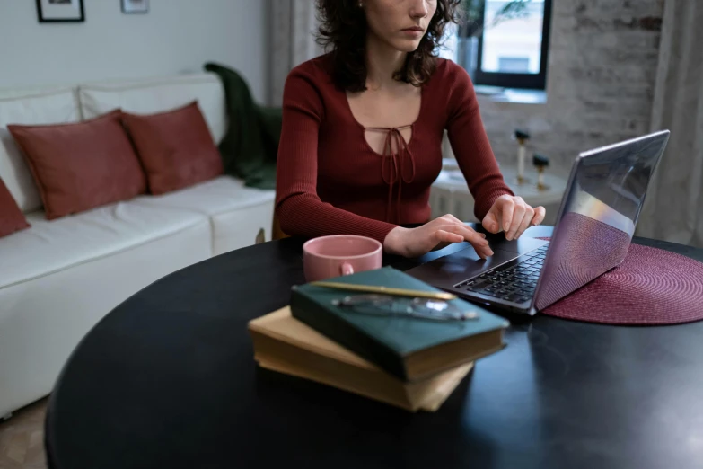 a woman sitting at a table using a laptop computer, trending on pexels, wearing a red outfit, wooden desks with books, brown, thumbnail