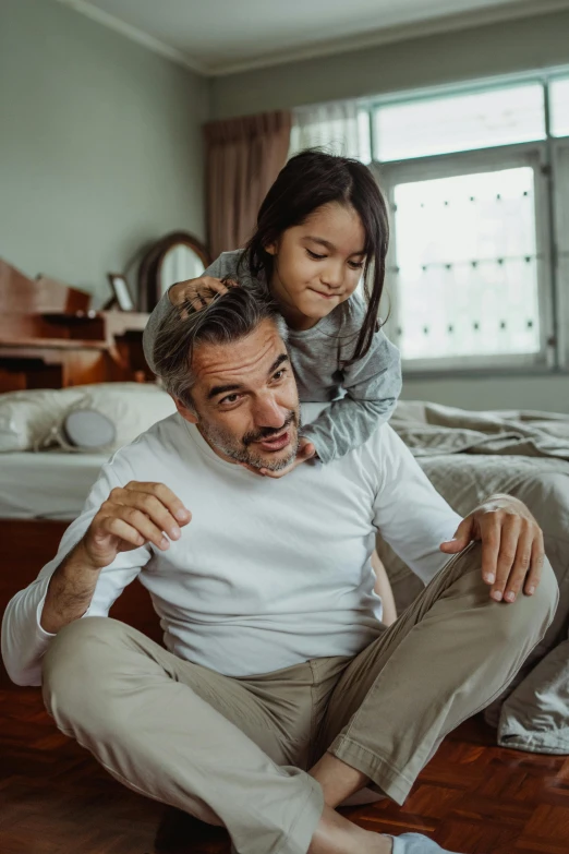 a man sitting on the floor next to a little girl, going gray, caring fatherly wide forehead, thumbnail, hispanic